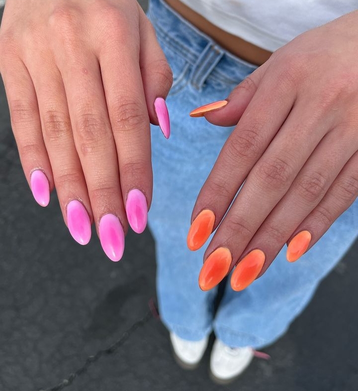 A pair of hands showing off orange and pink, almond-shaped aura nails